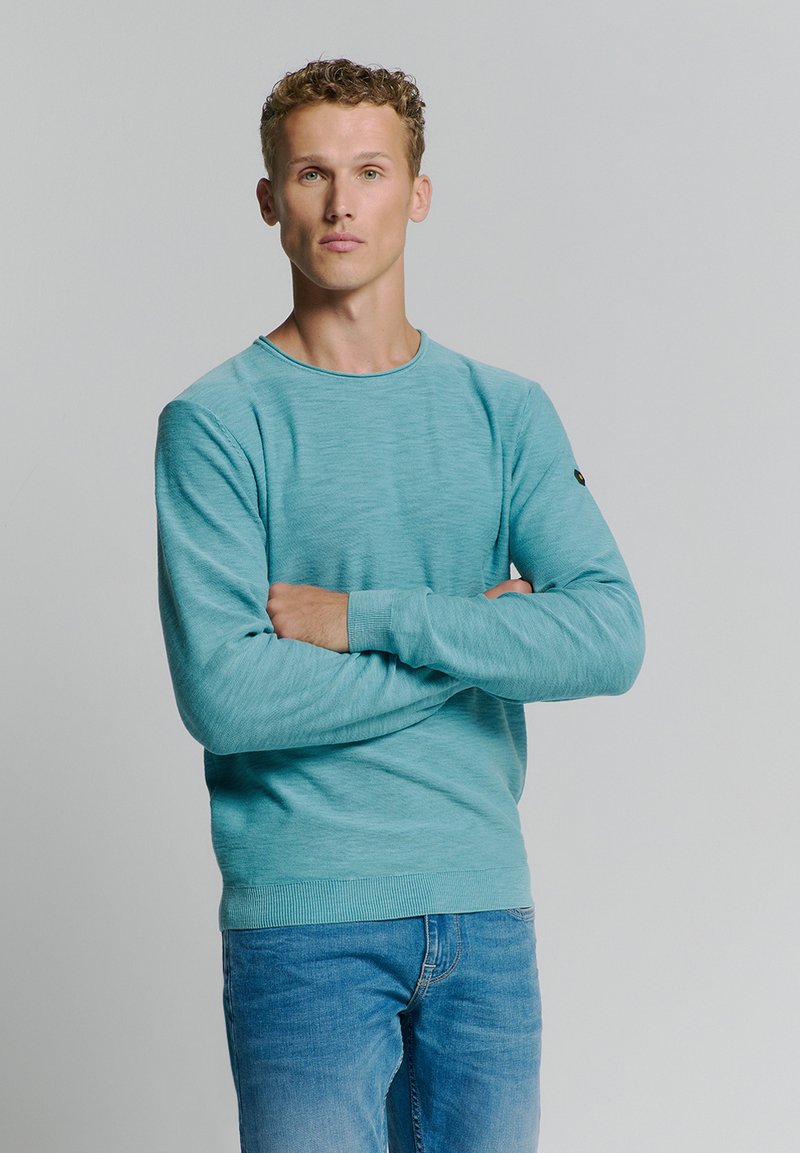 Lichtblauwe ronde hals trui met lange mouwen en gestructureerde stof. Gekozen in combinatie met denim jeans, wat een casual look toont.