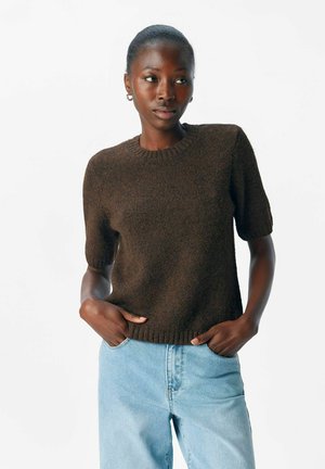 Braun gestrickter Kurzarmpullover mit Rundhalsausschnitt und strukturiertem Finish, kombiniert mit hellblauen Jeans.