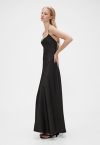 Črna maxi obleka iz satena s tankimi naramnicami, oprijetim zgornjim delom in razširjenim krilom, ki elegantno pada do tal. Preprost, eleganten dizajn.