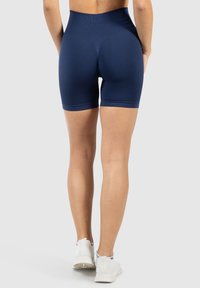 Náměsově modré šortky s vysokým pasem, s texturovaným vzorem a hladkým materiálem. Úzký střih končí uprostřed stehna. Bílé sportovní boty jsou viditelné dole.