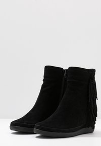 Černé semišové kotníkové boty se zipovým zapínáním, zdobené třásněmi po straně a texturovanou gumovou podrážkou pro lepší přilnavost.