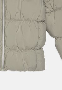 Ljust grå pufferjacka med kviltat mönster, dragkedjestängning och mjukt, texturerat tyg. Korta ärmar med samlade detaljer.