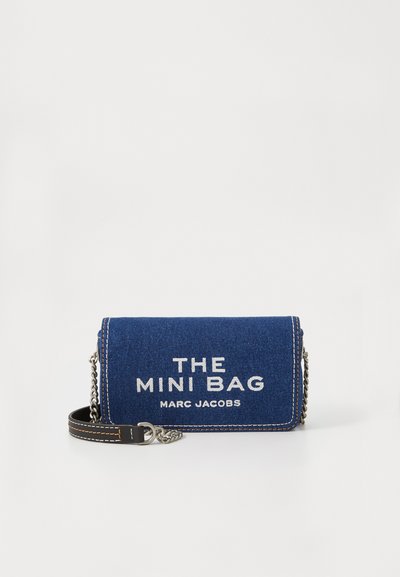 Sac mini en denim bleu foncé avec une chaîne argentée. Présente le texte blanc "THE MINI BAG" et "MARC JACOBS" à l'avant, avec des coutures contrastées.