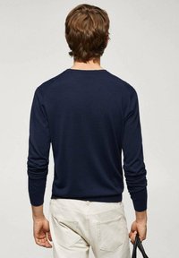 Pull à manches longues bleu marine avec un col rond, des poignets côtelés et une texture lisse, associé à un pantalon beige clair.