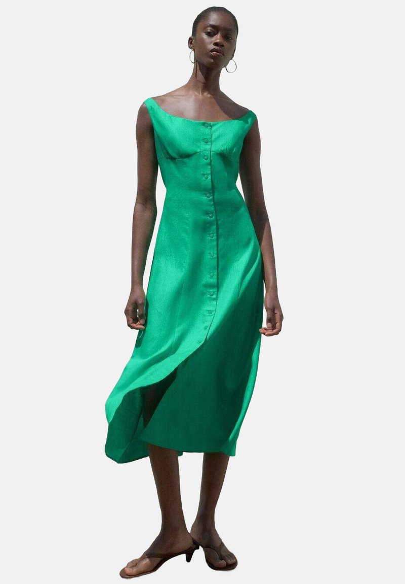Robe en lin vert avec une silhouette droite, décolleté bardot, fermeture à boutons sur le devant et fente sur le côté. Texture lisse et tissu léger.
