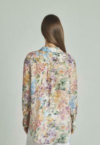 Blusa de manga larga de flores multicolores con una tela suave y ligera, que presenta un cuello clásico y detalles de botones en las mangas.