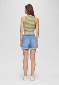 Groen gestreepte tanktop en lichtblauwe denimshorts met een relaxte pasvorm en elastische tailleband, gecombineerd met witte sneakers.