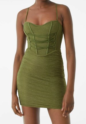 Robe verte en tissu texturé, avec un design ajusté, un décolleté en cœur, des bretelles fines et des détails en lacets avec des accents dorés.