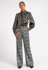Grijze satijnen blouse met een grote strik, poffige mouwen; gebloemde hoge taille wijde broek in blauw en crème; puntige zwarte schoenen.