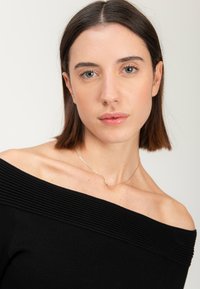 Top nero scoperto sulle spalle con texture a coste lungo il collo, abbinato a una sottile collana d'argento con un piccolo ciondolo.