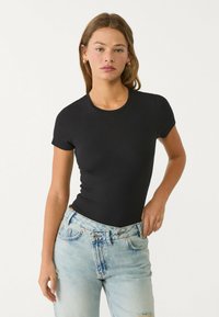 Črn bodysuit s kratkimi rokavi in okroglim izrezom, izdelan iz elastičnega materiala, v kombinaciji s svetlo modrimi uničenimi kavbojkami.