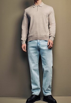 Polo de manga larga color gris claro con cuello de cremallera, combinado con jeans azul claro de pierna recta y zapatos negros gruesos. Textura suave, diseño casual.