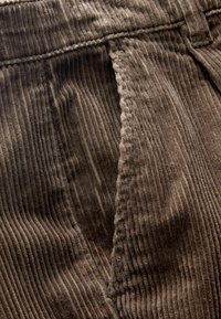 Bruin corduroy stof met een verticale ribbelstructuur. Bevat een zijzak en gestikte naden met een zachte, fluweelachtige feel.