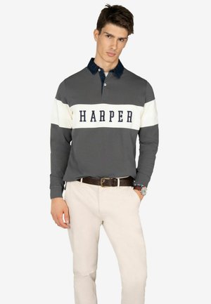 Polo gris de manga larga con una banda de rayas blancas y marinas que presenta "HARPER" en letras marinas. Combinado con pantalones beige y un cinturón marrón.