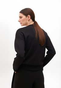 Black knit sweater with long sleeves, round neckline, and ribbed cuffs. Smooth texture with a relaxed fit and side seam detailing.