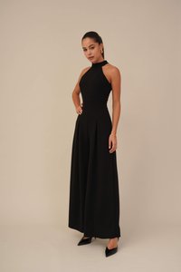 Black sleeveless jumpsuit featuring a high halter neck, fitted bodice, and wide-leg pants with pleats. Paired with black pointed-toe heels.