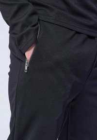 Pantalons de sport noirs en tissu texturé, comportant une poche zippée sur le côté et une coupe décontractée.
