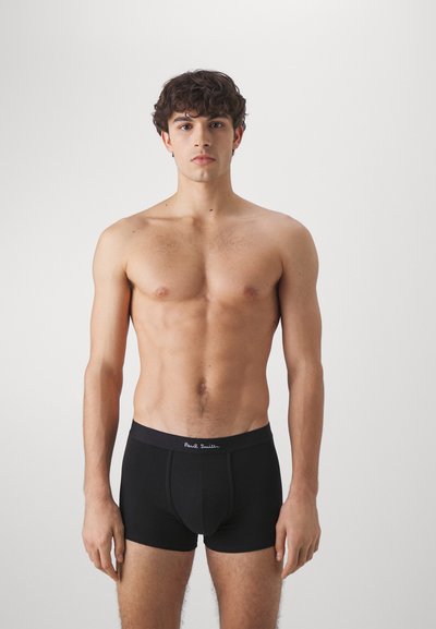 Boxers en coton noir avec une taille brodée de logo, design ajusté et texture lisse. Le modèle se tient de face.