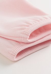 Tissu rose doux plié pour montrer des poignets côtelés et une texture tricotée lisse sur un fond clair.