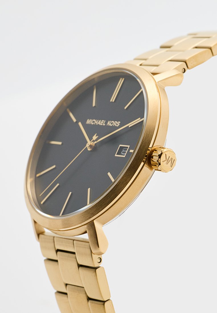 Montre en métal doré avec un cadran noir, design minimaliste, marqueurs d'heure, fenêtre de date et bracelet ajustable à maillons. Nom de la marque affiché.