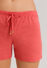 Pantalones cortos de algodón coral con cintura elástica, cierre de cordón y terminales en color dorado; textura suave y diseño casual.
