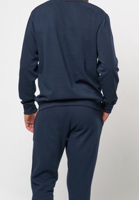 Mörkblåt träningsset i mjuk bomull; har långa ärmar och elastiska muddar, rundhalsad samt avslappnade byxor med elastisk midja.