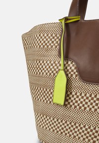Sac fourre-tout avec motif damier tissé beige et marron, bordure supérieure en cuir marron, et étiquette en cuir jaune néon attachée.