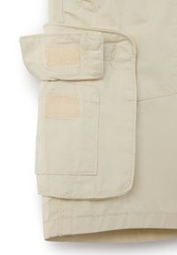 Bolsillo tipo cargo en color beige con cierres de gancho y bucle, con bordes cosidos y una textura suave. El diseño incluye secciones de tela en capas.