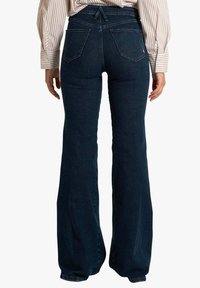 Jeans a zampa in denim blu scuro, con vita alta, due tasche posteriori e una finitura pulita. Tessuto liscio con dettagli di cucitura minimi.