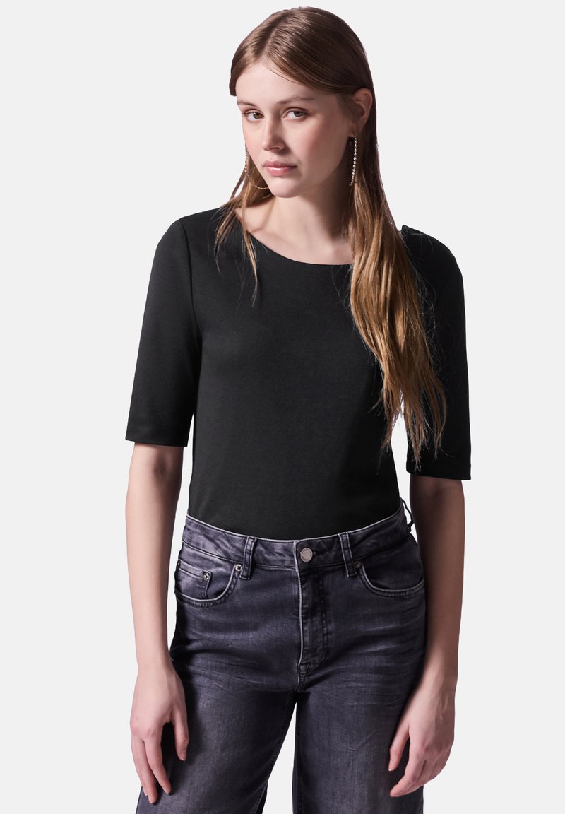Svart topp med korta ärmar, rund halsringning, textil med struktur. Matchas med mörkgrå jeans med framfickor och metalldekor.