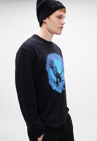 Tricou negru cu mânecă lungă, având un grafic cu un vultur albastru în centrul său. Materialul pare să fie bumbac, cu un guler rotund și o croială lejeră.