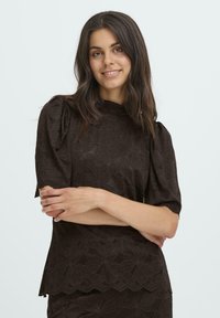 Brun blonde top med puf korte ærmer, høj halsudskæring, blomster mønster, bølget kant og en struktureret overflade.