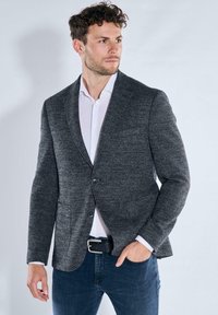 Dunkelgrauer Herrenblazer aus strukturiertem Stoff, mit Ein-Knopf-Verschluss, Revers mit Kerbe und zwei Vorderstaschen, getragen über einem weißen Hemd.