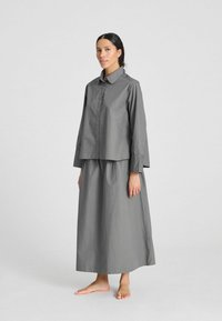 Camicia grigia con colletto, abbinata a una lunga gonna coordinata. Entrambi i capi presentano una texture liscia e una vestibilità comoda.