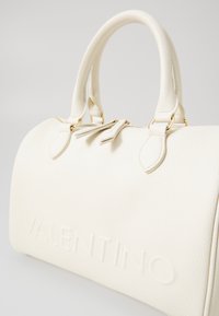 White pebbled leather handbag with structured shape, dual top handles, and gold hardware. Features embossed "VALENTINO" logo detail.