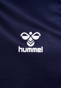 Marinefarget stoff med en glatt tekstur som har en hvit Hummel-logo, bestående av et stilisert bie-design og fet skrift.
