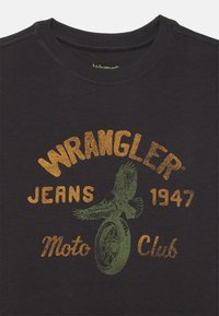 Μαύρο βαμβακερό t-shirt με λογότυπο Wrangler και απεικόνιση μιας κουκουβάγιας και ενός τροχού σε πράσινο και πορτοκαλί κείμενο. Στρογγυλή λαιμόκοψη, κοντά μανίκια.