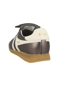 Retro-tyylinen Gola-tenniskenkä metallinvärisessä ruskeassa, jossa on valkoiset raidat, beige pohja ja kullanvärinen "Gola"-logo kantapäässä ja sivussa.