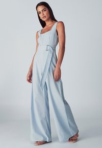 Combinaison bleu clair avec un décolleté carré, jambes larges et taille ceinturée. Fabriquée dans un tissu doux à la texture lisse.