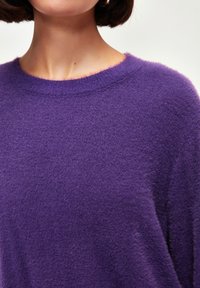 Lila gestrickter Pullover, weiche Textur, runder Ausschnitt, lockere Passform, sichtbare Fasern und dezente Bordüre am Kragen.