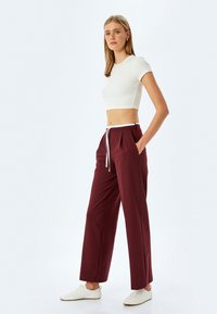 Pantalons larges bourgogne avec cordon blanc, dotés de poches latérales ; portés avec un crop top blanc ajusté et des baskets blanches. Texture lisse.