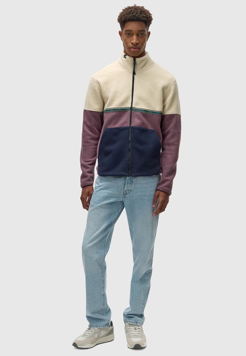 Chaqueta de forro polar con cuello alto, con paneles en crema, rosa y azul marino; cremallera completa; tejido texturizado; jeans de mezclilla azul claro; zapatillas beige.