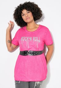 Růžové tričko s krátkým rukávem s nápisem "ROCK' N ROLL" ve stříbrném tisku, doplněné černým opaskem se cvoky. Kombinováno s distressed šedými džíny.