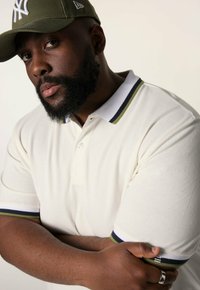 Vit polo skjorta med en texturerad finish, med en tvåknapps placket, accentuerad krage och ärmkanter i mörkgrön och marinblå ränder.