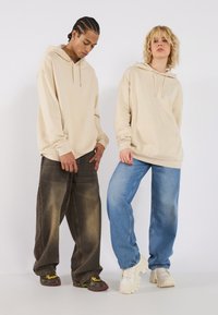 Beige hoodies with drawstrings worn over loose-fit dark and light blue jeans, paired with chunky sneakers in black, yellow, and white.