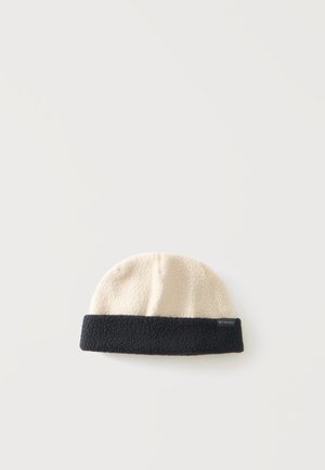 Fleece-Mütze mit cremefarbener Oberseite und schwarzem umgeschlagenem Rand, liegend auf einer weißen Oberfläche.