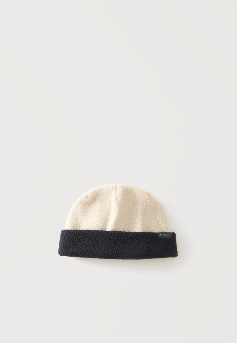 Bonnet en polaire avec dessus crème et bord noir replié reposant sur une surface blanche.
