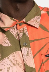 Kortærmet skjorte i orange og grøn stof med bladmønstre, prydet med en knap-ned krave og en brystlomme med et logo-tag.