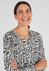 Cardigan a righe zebra in morbido tessuto, con maniche lunghe, scollatura rotonda e bottoni bianchi lungo il davanti. Colori bianco e nero.