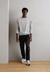 Sudadera gris, jeans negros y zapatillas blancas. El conjunto presenta un diseño sencillo con un cuello redondo y mangas largas.